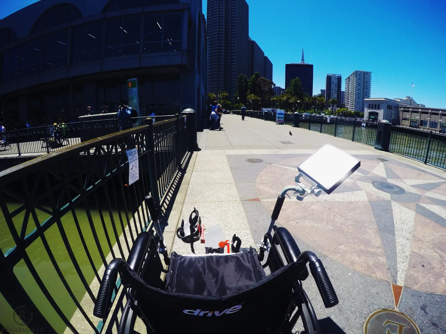Rear view of a manual wheelchair with LegMaker prototype pedals and a mounted control display outdoors